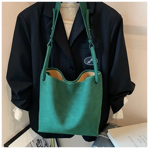 Detailansicht der grünen Tragetasche aus Mattleder mit Schultergurt vor schwarzem Blazer