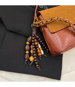 Detail of vintage brown leather bag with colorful wooden bead tassel and woven chain strap