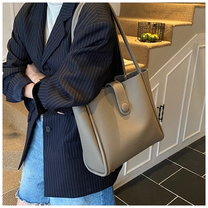 Detail view of khaki pebbled leather tote bag with long strap on a suit-clad model