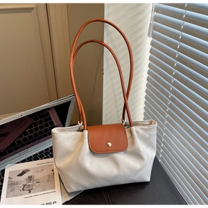 Detail of a minimalist tote bag featuring cream fabric and brown leather straps on a desk