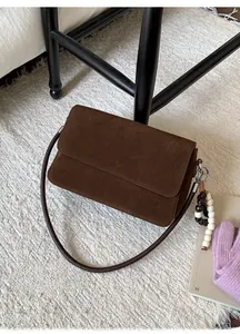 Close-up of brown suede crossbody bag with wood bead charm on a woven carpet