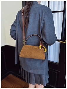 Detail of a brown suede pillow bag with leather straps and gold metal hardware for women