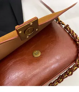 Detail view of the magnetic closure on a brown vintage crossbody bag with chain strap