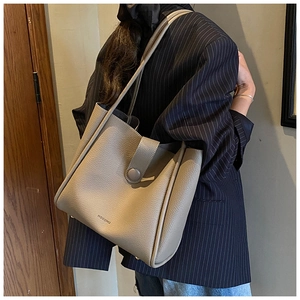 Detail of taupe pebbled leather tote bag showing HOCOMU logo and premium texture