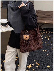 Detail view of large leopard print tote bag with brown plush bear charm and striped strap