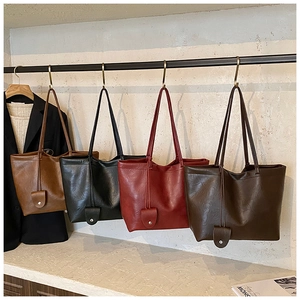 Detail of four suede tote bags in brown and black colors hanging on a minimal display stand