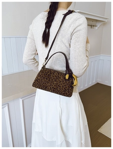 Leopard print pillow bag shown on model with brown leather handles and large gold metal ring