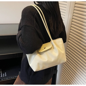 Detail of cream pleated tote bag with round magnetic buckle on a shoulder strap