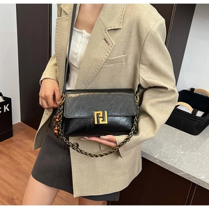Detail of a black crossbody bag with gold chain strap worn over a beige blazer