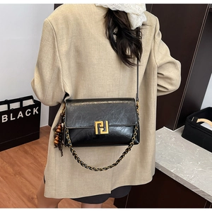 Detail of vintage black leather crossbody bag with gold buckle and tassel charm