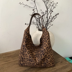 Close-up of leopard print hobo bag with brown leather strap on a rustic wood surface