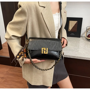 Detail of black leather crossbody bag featuring a golden lock and wooden bead tassel