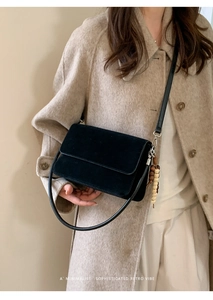 Detail of minimalist black matte shoulder bag with wooden bead charm and dual strap design