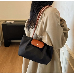 Detail of a black nylon tote bag with brown leather handles and envelope flap closure