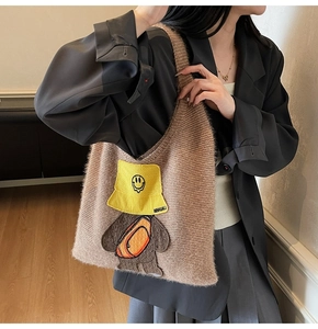 Close-up of brown plush tote bag featuring a cute cartoon bear patch with yellow hat