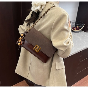 Detail view of brown shoulder bag featuring gold buckle and wooden bead charm on a model