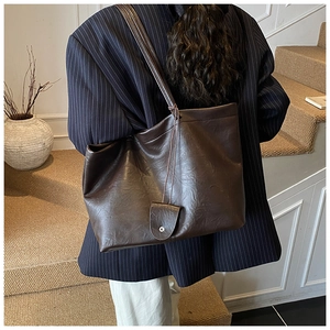 Detail of dark brown faux leather tote bag with distressed texture and small charm pouch