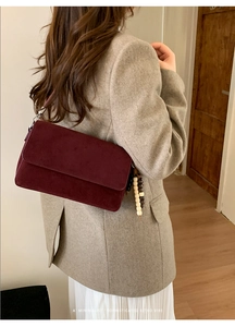 Detail of burgundy suede shoulder bag with wooden bead charm on a beige blazer outfit