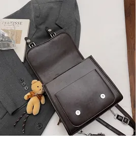 Detail of chocolate brown leather crossbody bag with silver hardware and plush bear charm