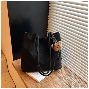 Detail of black corduroy tote bag with cute brown teddy bear charm on wooden surface