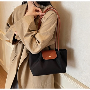 Detail of black nylon tote bag with brown leather flap worn over a khaki trench coat