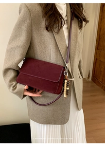 Detail of dark red suede crossbody bag featuring a wooden bead tassel and flap closure