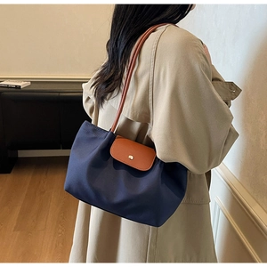Detail of navy nylon tote bag with brown leather handles and snap closure on beige trench coat