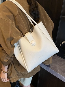 Chic off-white lychee grain leather tote bag worn by model over a velvet brown coat