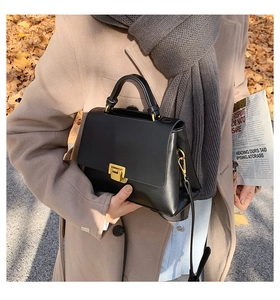 Détail d'un sac à main en cuir noir avec boucle dorée assorti à un manteau camel et une écharpe