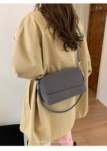 Detailed view of the dark grey matte leather shoulder bag worn by a model in a room