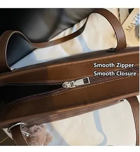 Detail view of a smooth metal zipper on a dark brown tote bag with a plush bear charm