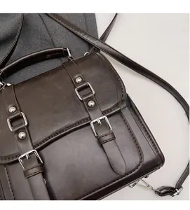 Detail of dark brown vintage faux leather messenger bag with silver buckles and studs