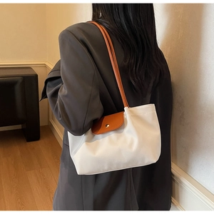 Detail of a white nylon tote bag with brown leather flap and handle worn by a model