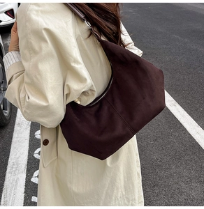 Macro van een bruine suède hobo-tas gedragen met een beige trenchcoat op straatbeeld