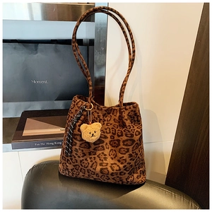 Detail view of large leopard print tote bag with plush bear charm on black chair