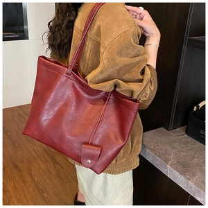 Detail view of large red suede tote bag with slim shoulder strap worn on person