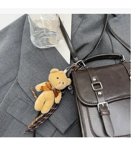 Detail of dark brown vintage crossbody bag with a plush bear charm on grey blazer