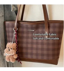 Close-up of brown plaid tote bag with plush puppy charm and metallic detail