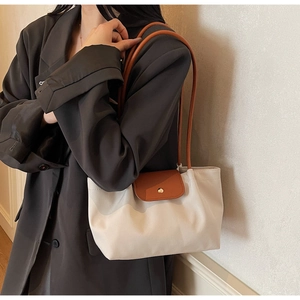 Close-up of beige tote bag with brown leather flap and gold metal clasp on model