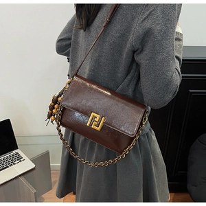 Detail view of a vintage brown leather crossbody bag with gold buckle and beaded charm