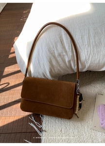 Detailed view of brown suede crossbody bag with wood bead and black tassel charms