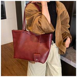 Detailed view of a spacious burgundy tote bag in PU leather worn by a model in a room