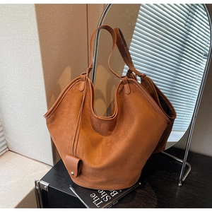 Détail d'un sac cabas en daim marron avec coutures soignées et pendentif sur bois sombre