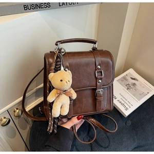 Detail view of retro brown leather bag with metallic buckles and a plush bear pendant