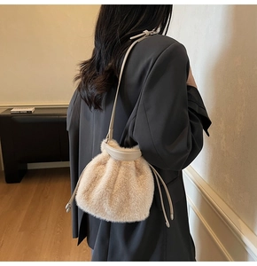 Detail of beige faux fur bucket bag featuring a leather handle and drawstring closure