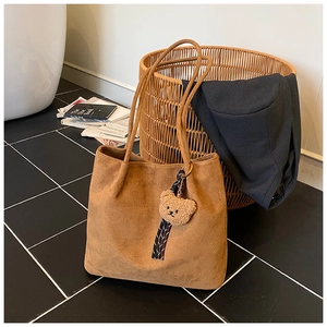 Detail of a brown suede tote bag featuring a cute plush bear charm with striped ribbon