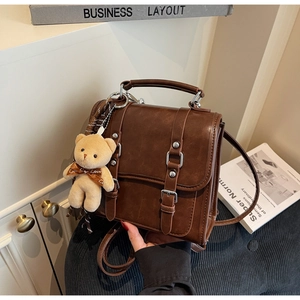 Close-up of retro dark brown leather satchel with dual straps and plush bear charm