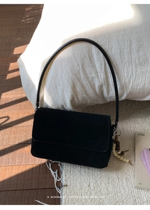 Detail of black suede flap bag with vintage wood bead tassel on plush carpet background