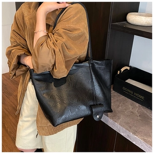 Detail of a large black pleated leather tote bag with a small pouch on a model