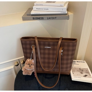 Detailed view of brown checkered tote bag with a metallic plate and plush bear charm